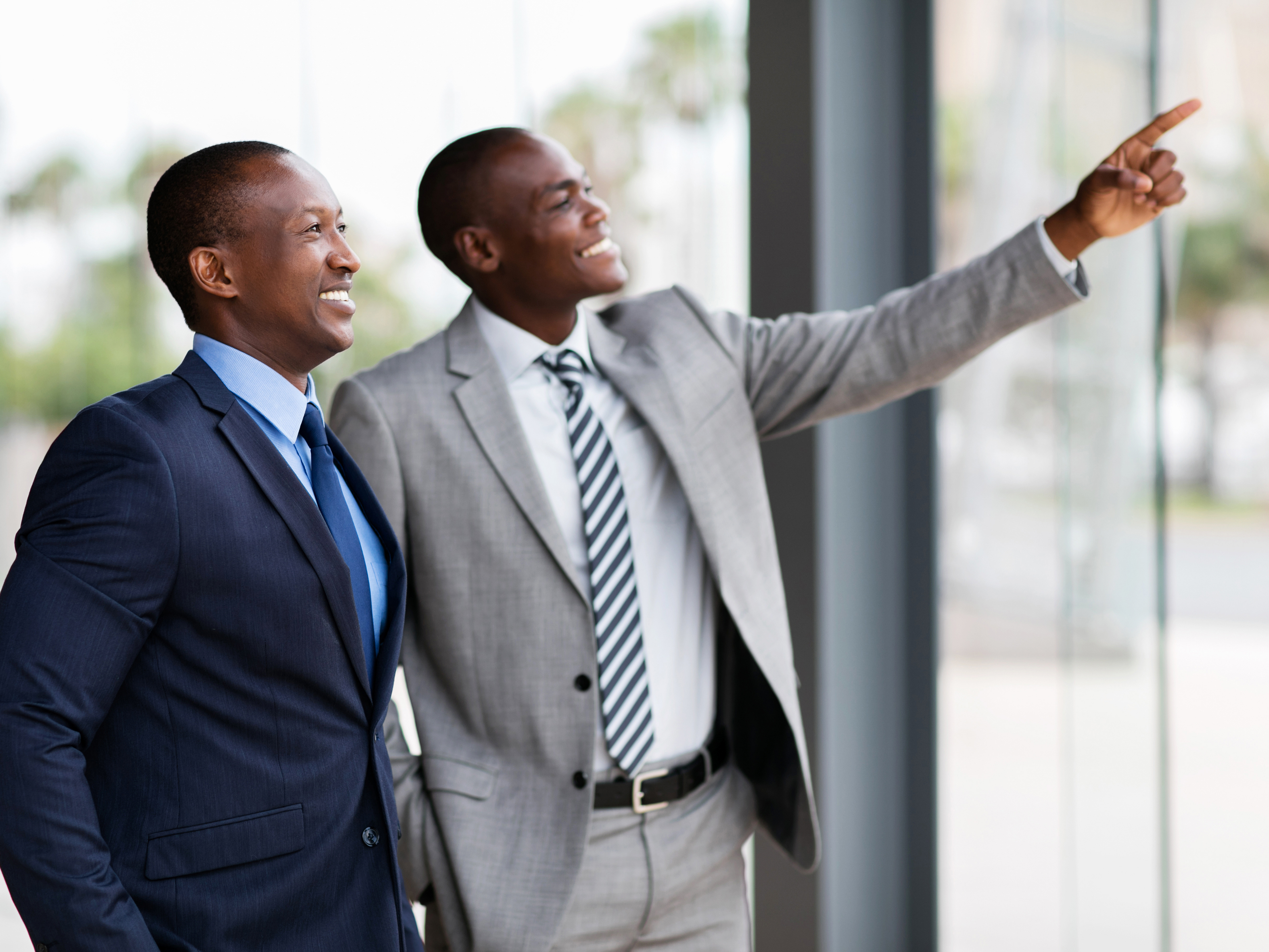 Two Black business leaders reviewing plans near a window with city views