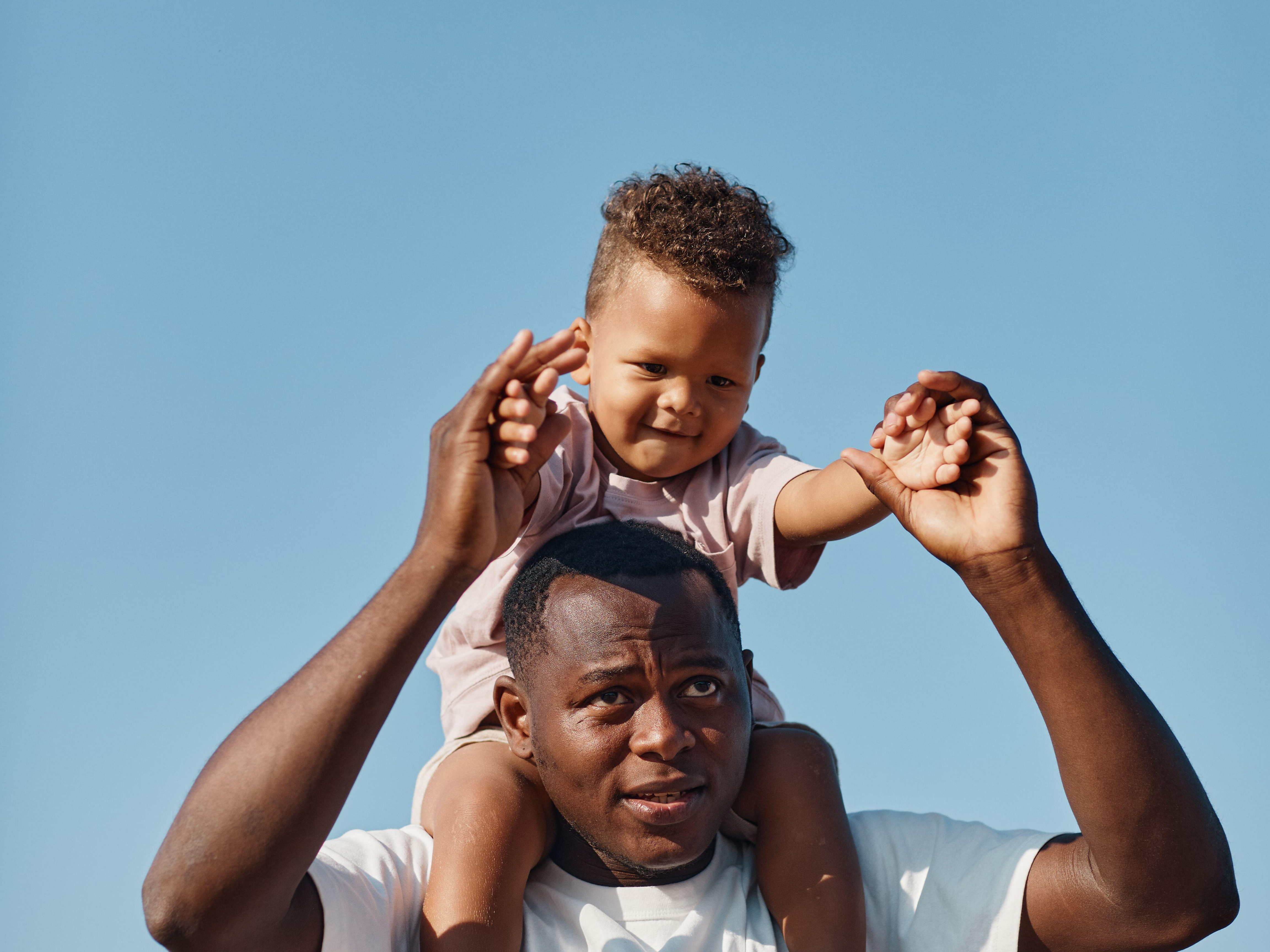 Father carrying his son on his shoulders against a blue sky
